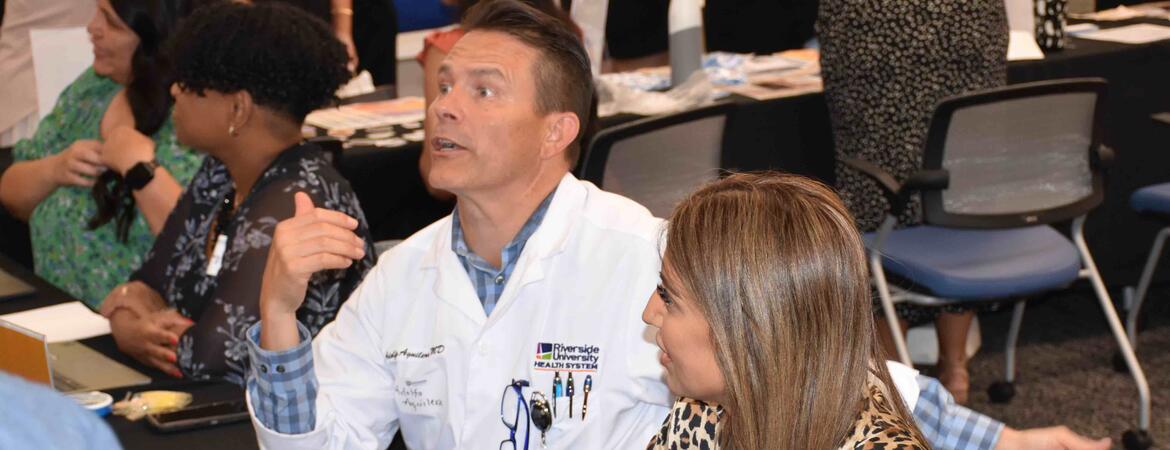 Dr. Aguilera in a white coat sitting at a table at orientation 2024