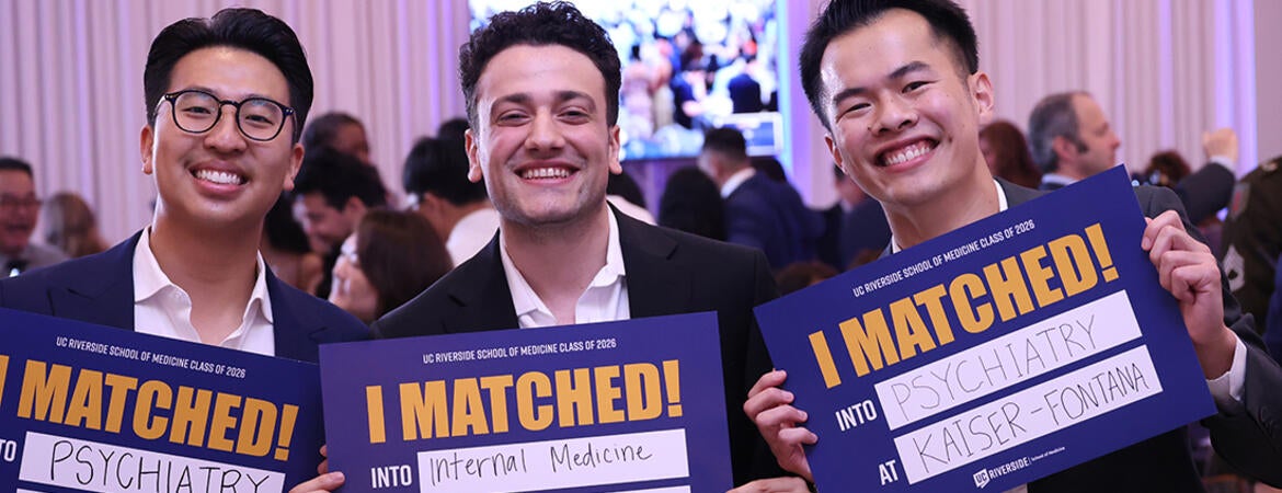 Three medical students hold up signs saying where they will be going for residency.