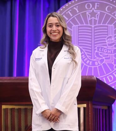 Pamela Munoz wearing her white coat in front of the UCR seal