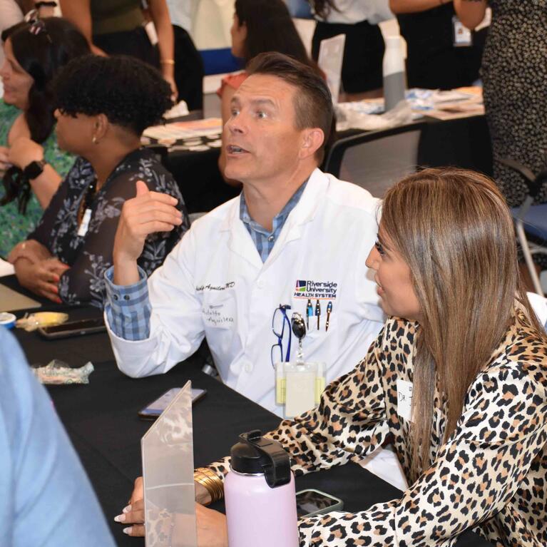 Dr. Aguilera in a white coat sitting at a table at orientation 2024