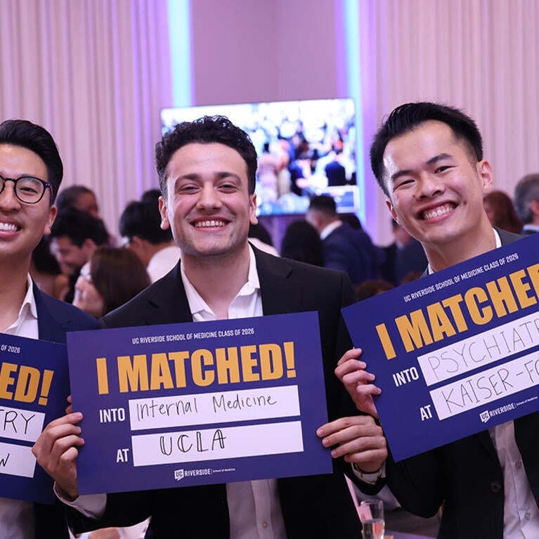 Three medical students hold up signs saying where they will be going for residency.