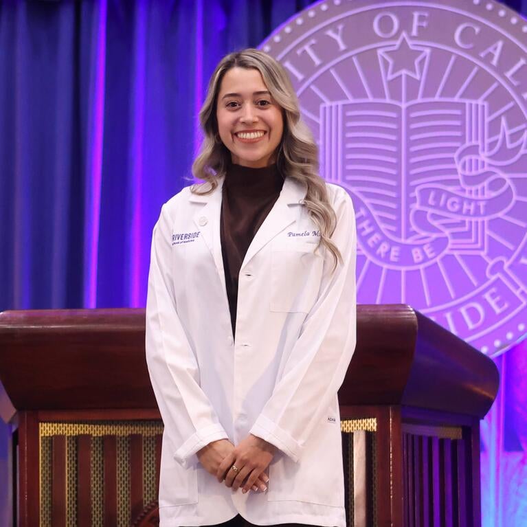 Pamela Munoz wearing her white coat in front of the UCR seal