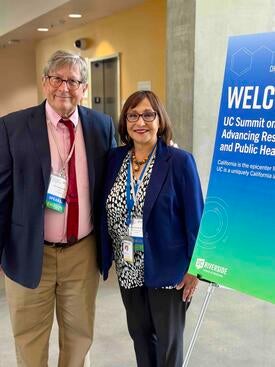 Dr. Shoptaw and Dr. Bholat next to a sign for the UC Summit on Methamphetamine