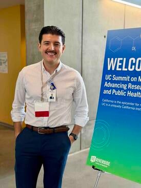 Mario Navarro stands next to a sign for the UC Summit on Methamphetamine